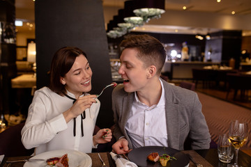 young caucasian married couple treating food with each other in restaurant. happy man and woman try delicious tasty food, dessert cooked by professional cook