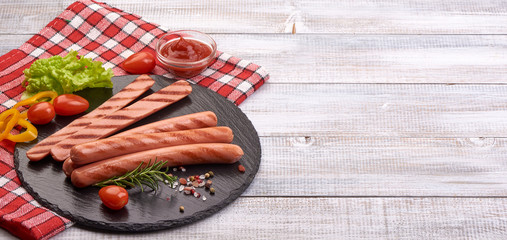 Grilled sausages with spices and herbs on a stone plate, on rustic background
