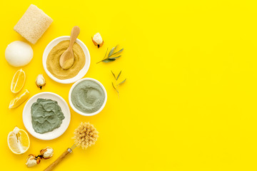 Natural spa concept with various cosmetic clays. Composition with healing herbs, wooden massage brush on yellow table, flat lay, space for text