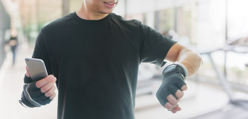 Asian athletes man wearing fitness gloves are resting after exercising. And use a smartphone with smartwatch to checking health data.Concept of sport and technology.