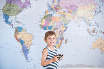 happy delightful little kid in striped sailor tank top holding vintage film camera on world map...