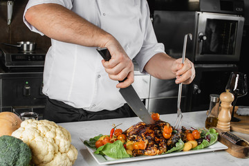 cropped professional cook in apron cut cooked meat for restaurant visitors, chef-cooker beautifully decorates a plate in kitchen. culinary, gourmet concept