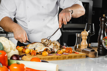 caucasian chef-cooker in white apron cut cooked meat in kitchen, prepare beautiful dish for restaurant visitors. man use sharp knife