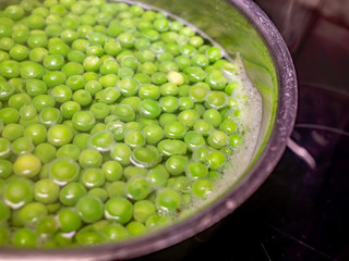 Frozen garden peas boiling in a stainless steel saucepan on the cooker hob