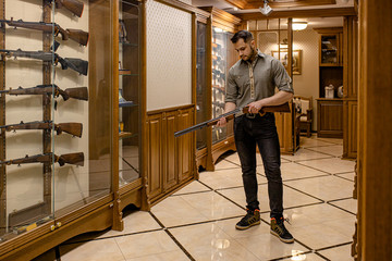 caucasian customer inspecting rifle in guns store, he liked this firearm, want to buy it for hunting