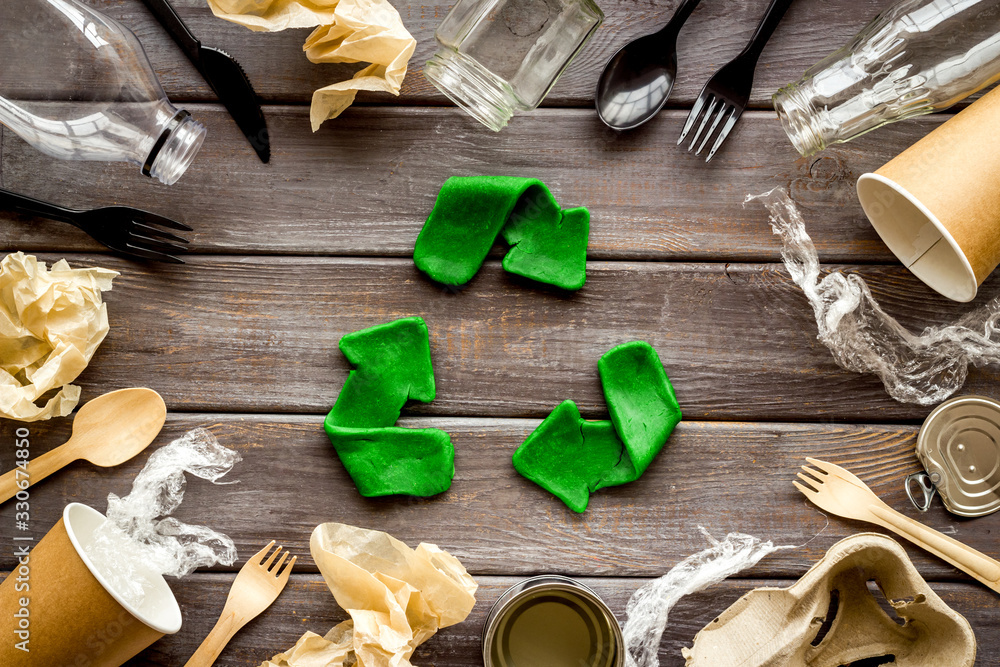 Poster Recycle concept. Green arrows icon among waste on dark wooden background top-down