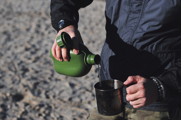 Water is pouring from an army canteen battle flask into a mug.