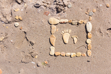 touching picture of sea pebbles on  sandy beach. Image of a child's and adult's foot made of stones. Ebbles and sand in the sea. Card. Background.
