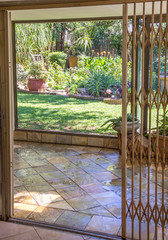 View from inside through an open sliding door to a veranda and a lush green garden image in vertical format