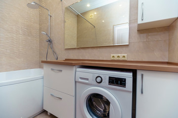 bathroom with brown washbasin and countertop, white cabinets, large mirror, washing machine,toilet. Beige wall tiles