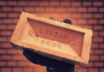 Hand hold red brick against brick wall