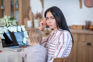 Young mom holding daughter, interfering with her work