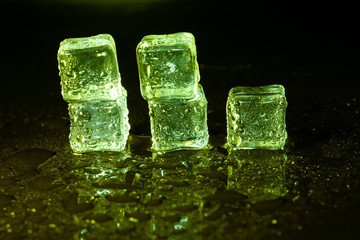 Green ice cubes on black table background.