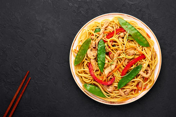 Chicken Lo Mein in white plate at dark slate background. Lo Mein is Chinese cuisine dish with chicken meat, egg noodles, vegetables and sauces. Chinese Food. Stir Fried Noodles. Copy space
