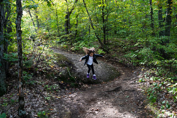 Fototapeta na wymiar young girl jumping from rock in forest in autumn in park, slow shutter, motion blur. Gatineau Park, Quebec, Ontario.