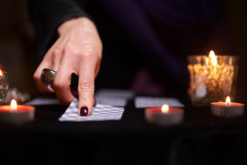 Close-up of fortune teller divining on cards sitting at table with burning candles, magic ball