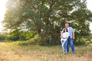 Fototapeta premium Pregnant woman and husbant kiss on the field. Happy people love spending time together in the nature