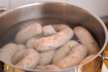Making bavarian white sausages at home, chain of sausages  boiling in pot with hot water