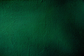 A grungy background of dark mint color with dimming. Dark mint colored uneven surface for design and text.