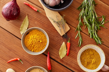 food, culinary and eating concept - bowls with different spices, onion, garlic and red hot chili peppers on wooden table