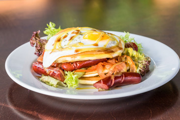 Pancakes with grilled sausages, egg, salad drizzled with sauce on a white plate