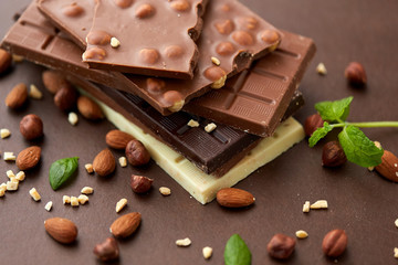 sweets, confectionery and food concept - bars of dark, white and milk chocolate with nuts on brown background