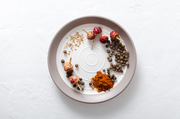 Obraz na płótnie Canvas Top view of plate and different kinds of pepper.Red pepper flakes, dry red pepper, black peppercorns on the plate, white surface