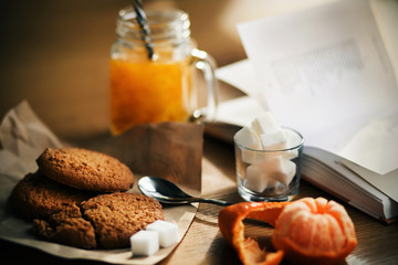 On the wooden table the morning Breakfast - warm sea buckthorn morse in a glass mug, oatmeal cookies, half-peeled tangerine and lump sugar in a Cup, and next to it lies an open book with poems. ©  Valeri Vatel