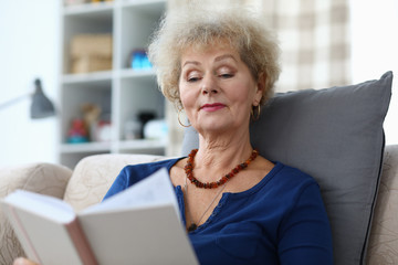 Portrait of concentrated smiling female reading hardcovered book. Good-looking attractive senior...