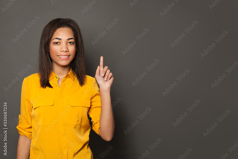 Wall mural happy african american woman pointing up on gray banner background