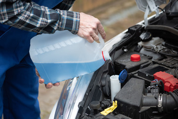 Hands of mechanic pouring windshield washer fluid in a car