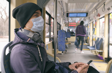 Adult man with medical protective mask and gloves inside public transport tram using smartphone....