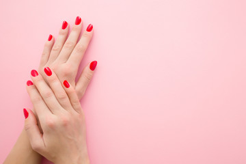 Beautiful woman hands with red nails on light pink table background. Pastel color. Manicure beauty...