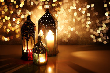 Ornamental Arabic lanterns with glittering bokeh lights. Burning candles on table glowing at night....
