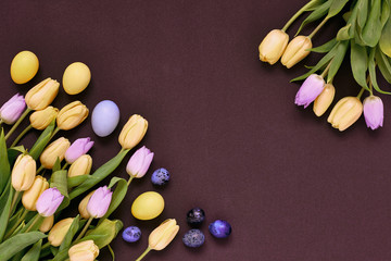 Yellow and lilac tulip flowers with easter eggs on dark background.
