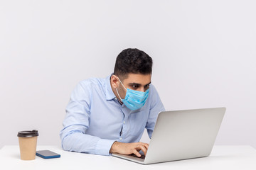 Flu-sick workaholic office employee in hygienic mask working on laptop, using protect filter against contagious disease coronavirus, looking crazy about his job in spite epidemic. studio shot isolated