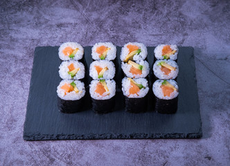 Maki rolls with salmon and avocado on a slate plate with concrete background. Japanese cuisine.