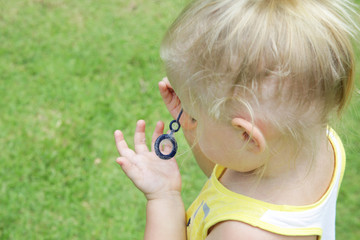 Happy little toddler girl blowing soap bubbles in the park