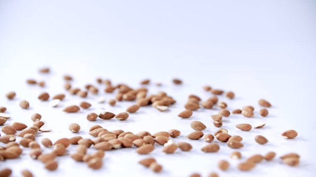 handfull of unroasted almonds fall and bounce on a white reflective background shallow depth of field, slow motion