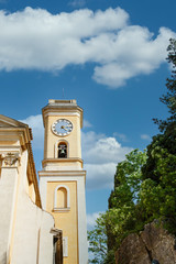 A yellow stucco clock tower into blue sky in Eze, France