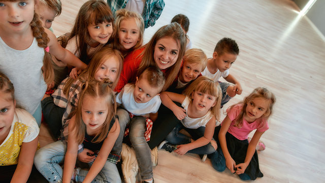 Posing together. Happy female dance trainer with positive and cute children looking at camera and smiling while sitting on the floor in dance studio