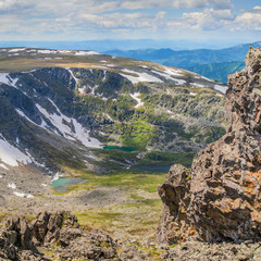 Over the mountain gorge. Rocky slopes, snowfields and small lakes. Spring in the mountains.