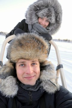 Smiling girl and boy portrait on dog sled in snow landscape, Lapland, Finland