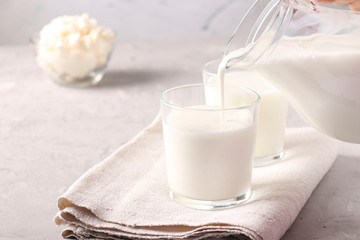 Kefir or Ayran fermented drink is poured into a glass from a jug, as well as cottage cheese in a bowl on a light gray background, Copy space