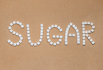 inscription text word sugar with white cubes of refined sugar on a background of craft paper