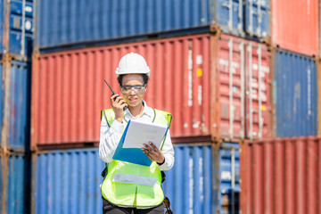 Woman Foreman in hardhat and safety vest holding holding clipboard checklist and talks on two-way...