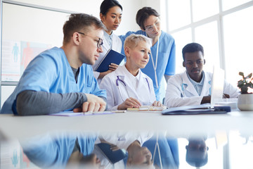 Low angle view at multi-ethnic group of doctors looking at laptop screen while working together...