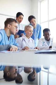 Multi-ethnic Group Of Doctors Looking At Laptop Screen While Working Together Sitting At Desk In Medical Office Interior, Copy Space With Reflection