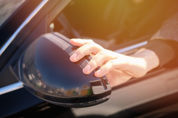 Hand adjusts the side view mirror of car.