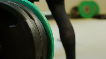 A young small caucasian man in black workout clothes picks up two green heavy weights and places one on the each side on a bench press at a fitness gym for a workout.
